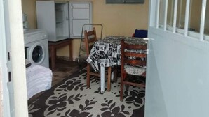 A compact kitchen with a washing machine, a table with a patterned tablecloth, and a window with a view of greenery.