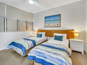 Habitación doble con dos camas, un cuadro de una playa y una ventana con persianas.