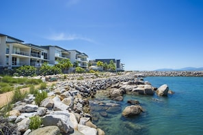 Un hôtel situé en bord de mer, doté de nombreux balcons, d’une côte rocheuse et d’une eau d’un bleu cristallin.