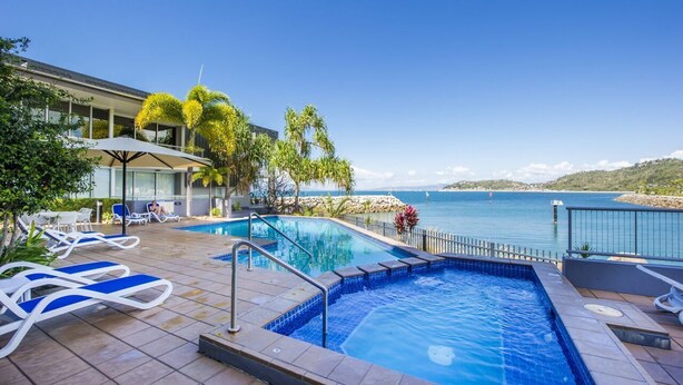 A pool area with lounge chairs, a glass-enclosed building, and a view of the sea. - 1 Bright Point Apartment 2204 (Nelly Bay)