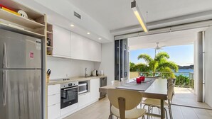 A modern kitchen with stainless steel appliances, a dining area with a table and chairs, and a view of the sea through large windows. - 1 Bright Point Apartment 2204 (Nelly Bay)