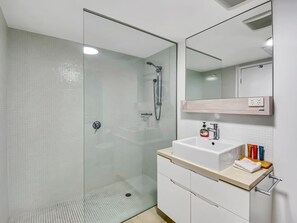 Ein modernes Badezimmer mit einer gläsernen Duschkabine, einem weißen Waschbecken mit Spiegel darüber und einer Holzauslage.