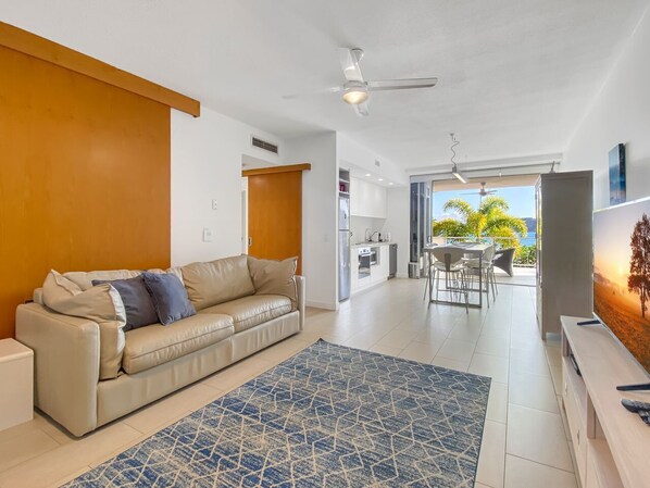 A living room with a sofa, a patterned rug, a ceiling fan, and a view of the outdoors. - 1 Bright Point Apartment 2204 (Nelly Bay)