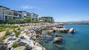 A beachfront hotel with multiple balconies, a rocky shoreline, and clear blue water. - 1 Bright Point Apartment 2204 (Nelly Bay)
