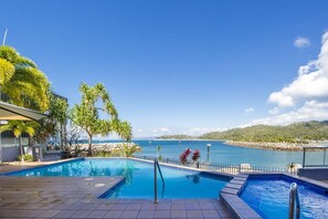 Una piscina con vista al mar, rodeada de palmeras y un edificio.