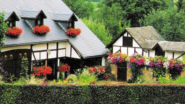 Ein traditionelles Fachwerkhäuschen mit Blumenkästen am Dach und einem gepflegten Garten.