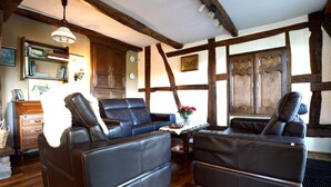 Ein gemütlicher Raum mit zwei Ledersofas, Holzbalken, einem Bücherregal und einem Holzschrank.