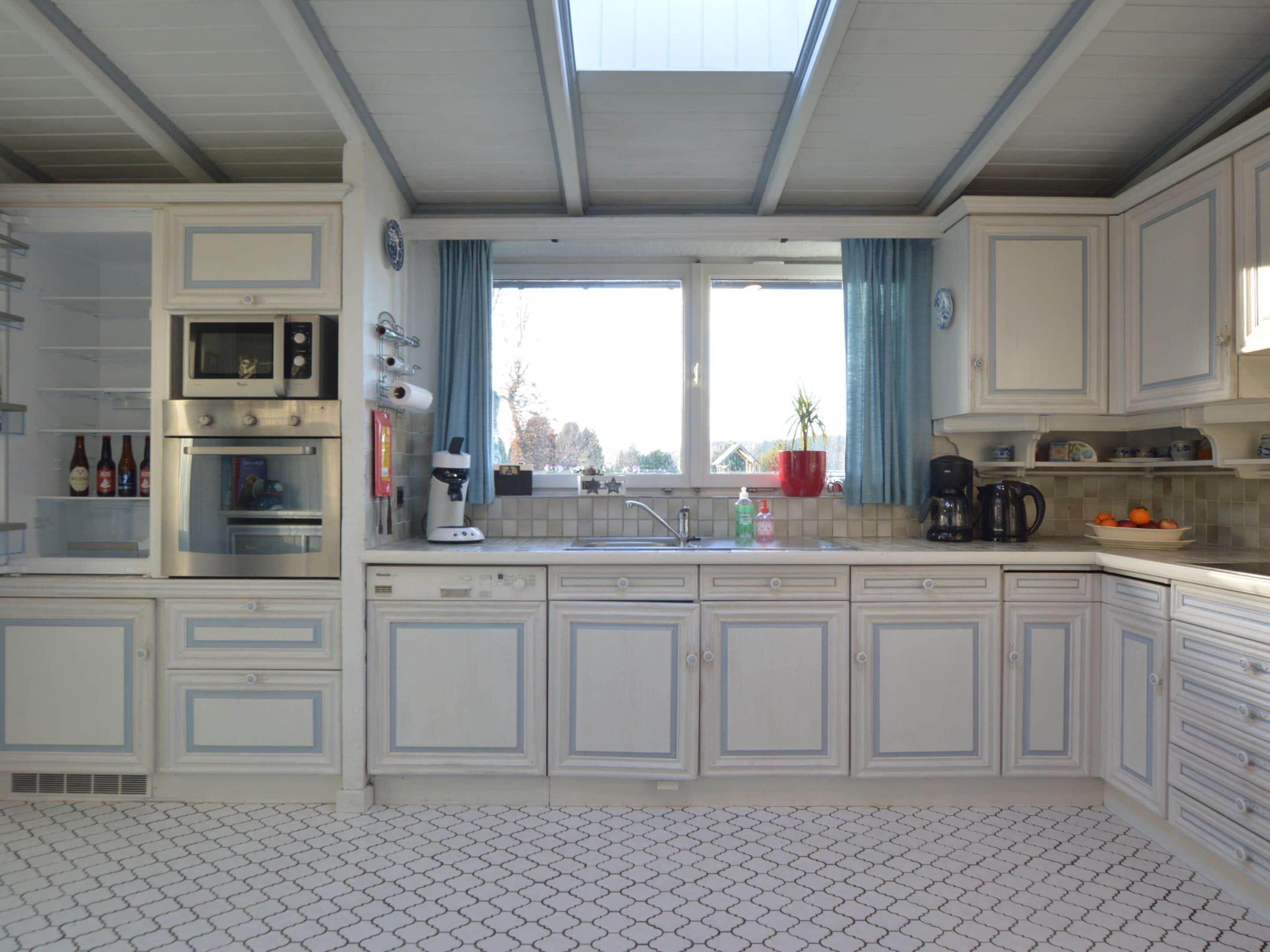 A kitchen with white cabinets, a microwave, an oven, a sink, and a window with curtains.