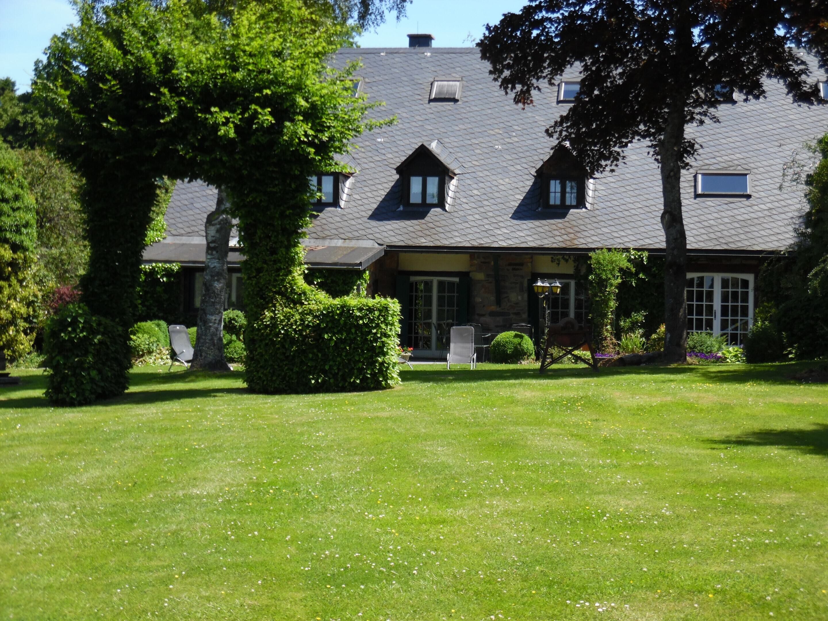 A large house with a sloped roof, a well-maintained lawn, and a garden with various plants and flowers.