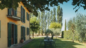 Une cour avec une table et des chaises, entourée d’une pelouse bien entretenue et d’arbres.