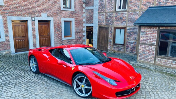 A red sports car parked in front of a brick building with multiple doors and windows.
