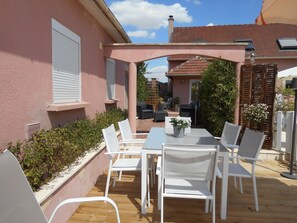 Un patio con sillas blancas y una mesa, rodeado por un muro rosa y una terraza de madera.