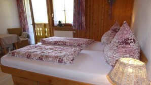 Uma cama de madeira com roupa de cama florida, um candeeiro de vime e um tapete com padrão geométrico.