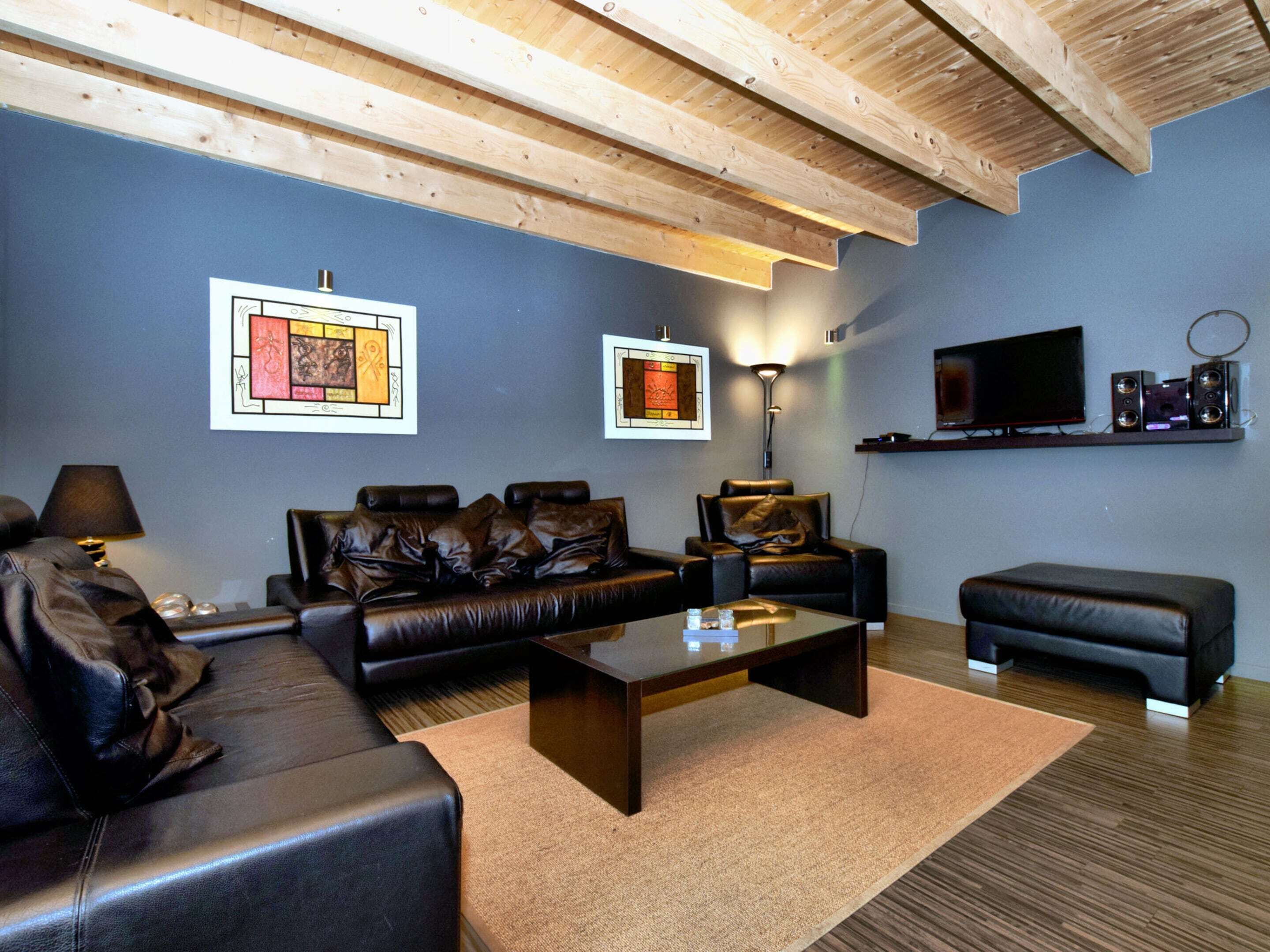 A living room with a dark blue wall, two leather sofas, a glass coffee table, a floor lamp, a TV, and a shelf with speakers.