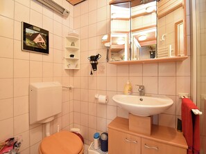 A bathroom with a toilet, sink, mirror, shelves, and a picture on the wall. - Ferienhaus in Brigach (Sankt Georgen im Schwarzwald)