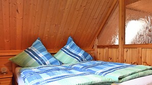 A wooden cabin room with a bed, two pillows, a window, and a wooden wall. - Ferienhaus in Brigach (Sankt Georgen im Schwarzwald)