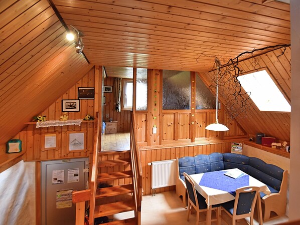 A cozy attic room with wooden walls, a loft bed, a dining table with chairs, and a small kitchenette. - Ferienhaus in Brigach (Sankt Georgen im Schwarzwald)