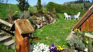 A wooden staircase leading to a garden with a table and chairs, surrounded by greenery and flowers. - Ferienhaus in Brigach (Sankt Georgen im Schwarzwald)