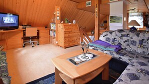 A cozy room with a wooden ceiling, a television, a desk, a bookshelf, a patterned sofa, and a lamp. - Ferienhaus in Brigach (Sankt Georgen im Schwarzwald)