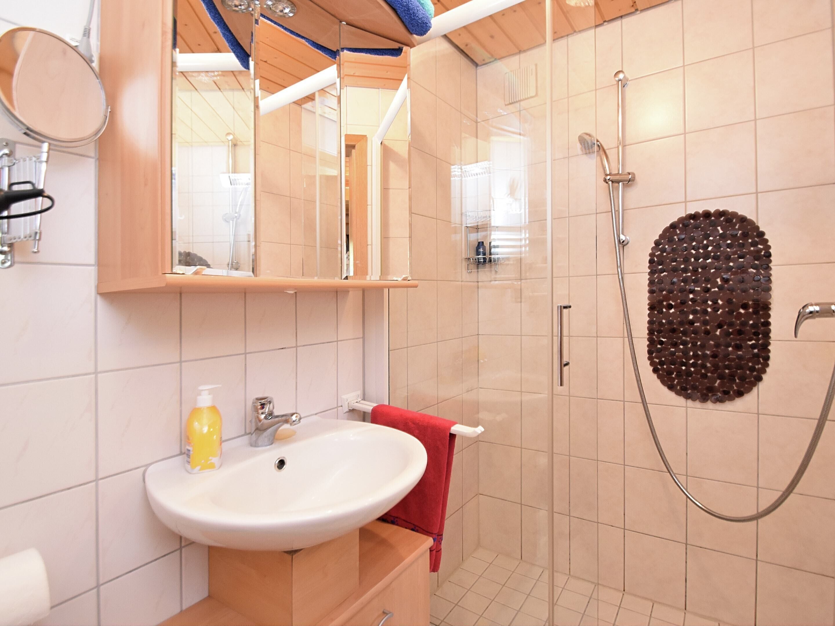 A bathroom with a sink, mirror, shower, and tiled walls.