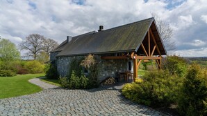 Une charmante maison en pierre avec un porche en bois, entourée d’un chemin pavé et d’une végétation luxuriante.