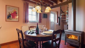 Un coin repas avec une table ronde, des chaises, une bouteille de vin et un poêle à bois.