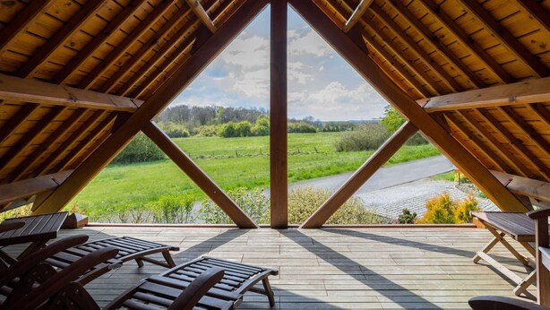 Une chambre mansardée avec un plafond en pente en bois, une vue sur un champ verdoyant et plusieurs fauteuils en bois.