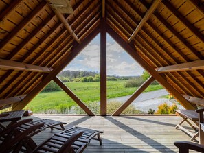 Une chambre mansardée avec un plafond en pente en bois, une vue sur un champ verdoyant et plusieurs fauteuils en bois.