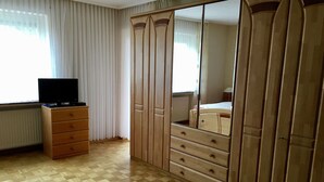 A bedroom with a wooden wardrobe, a dresser, a television, and a window with curtains. - Unterkunft mit Zwei Baeder in Lirstal (Lirstal)