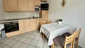 A compact kitchen with wooden cabinets, a microwave, a stove, and a dining table with chairs. - Unterkunft mit Zwei Baeder in Lirstal (Lirstal)