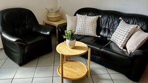 A black leather sofa with patterned cushions, a small wooden side table with a woven basket, and a round wooden table with a plant. - Unterkunft mit Zwei Baeder in Lirstal (Lirstal)