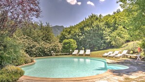 Una piscina con sillones de descanso, rodeada de vegetación y con montañas al fondo.