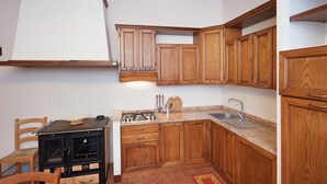 Una cocina con armarios de madera, estufa a gas, pileta y una silla.