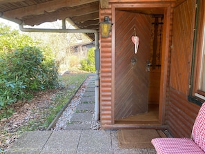 A wooden cabin with a large door, a small porch area, and a checkered bench. - Dog-friendly Holiday Home in the Knull (Neuenstein)