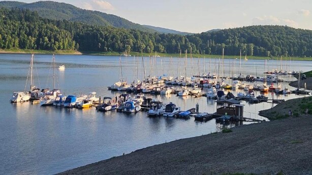 A marina with numerous boats docked, surrounded by forested hills.