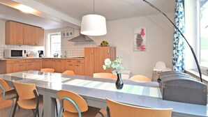 A modern kitchen with wooden cabinets, a central island with chairs, a hanging light, and a vase with flowers.