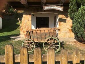 A rustic wooden building with a stone facade and a wooden cart in front. - Ferienwohnung in Kamschlacken (Osterode am Harz)