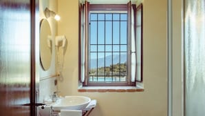 A bathroom with a wooden ceiling, a window with curtains, a sink, a toilet, and a mirror with lights. - Belvilla by OYO Bilo Grande Della Cascina (Salò)