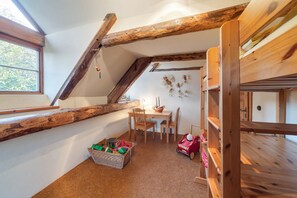 A cozy attic bedroom with exposed wooden beams, a wooden bunk bed, a desk with chairs, and a toy car.