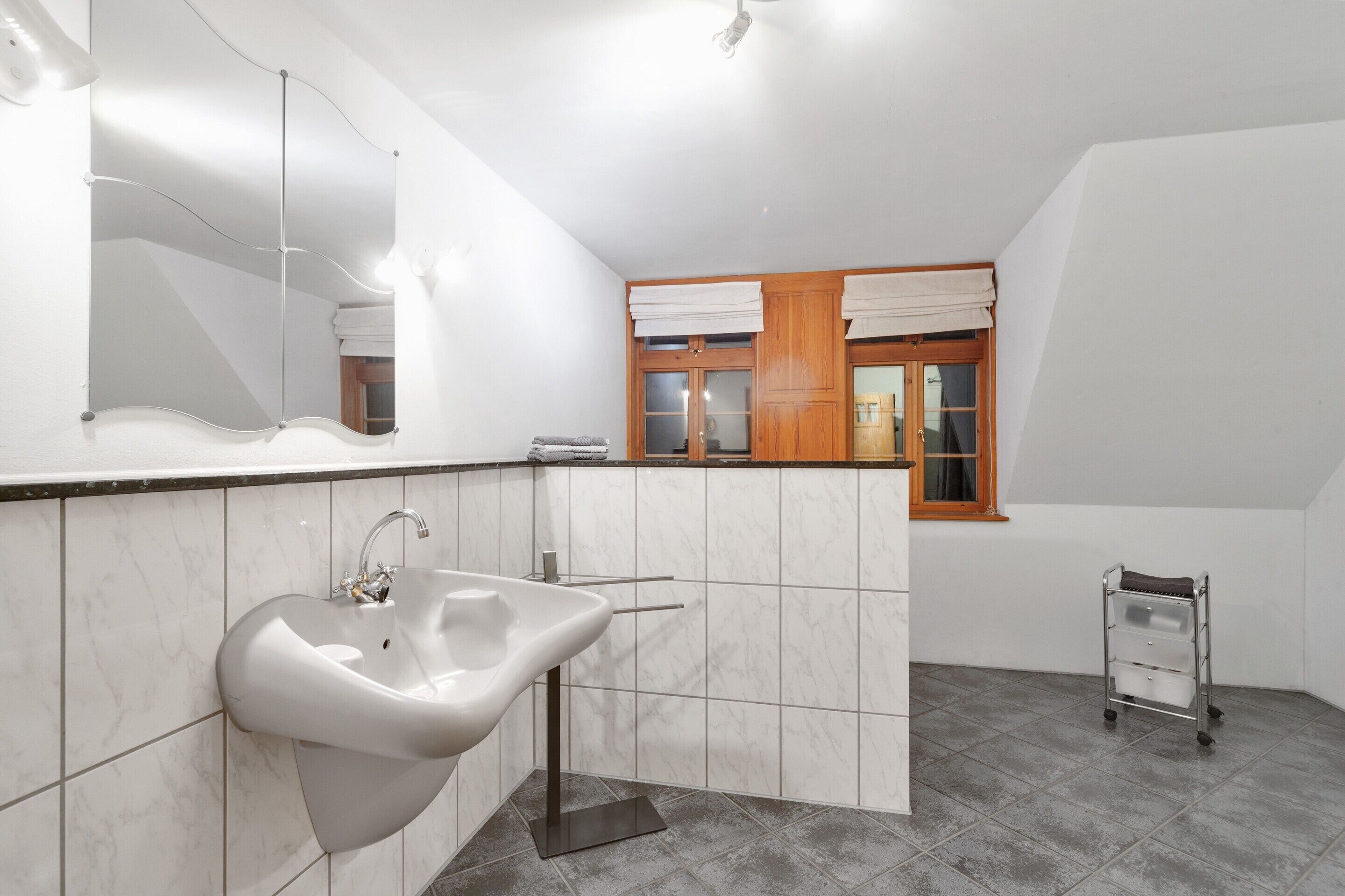 A bathroom with a white sink, a mirror, and a window with curtains.