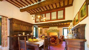 A traditional dining room with a wooden table, chairs, and a chandelier. There is a fireplace with antlers above it, and a large cabinet with a vase on top. - Belvilla by OYO La Provincia (Montecatini Val di Cecina)