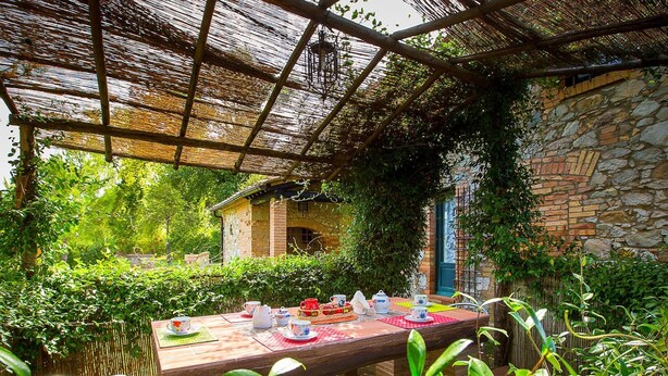 An outdoor dining area with a table set for tea, surrounded by greenery and a stone building. - Belvilla by OYO La Provincia (Montecatini Val di Cecina)
