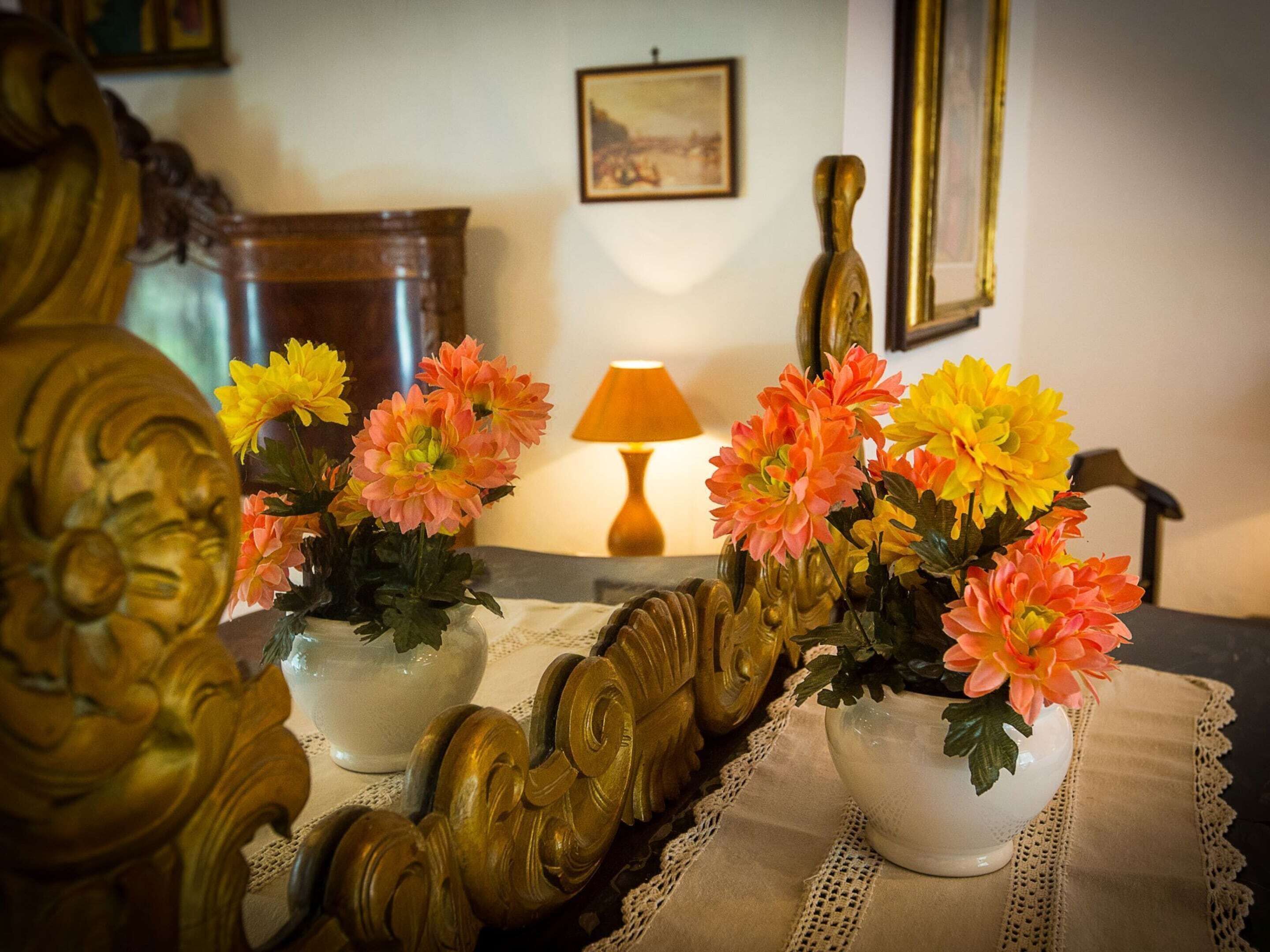 A room with a bed, two white vases with flowers, a lamp, and a framed picture on the wall.