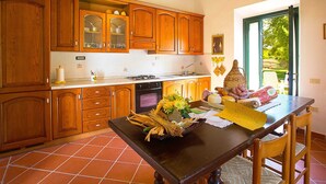 A kitchen with wooden cabinets, a stove, and a dining table with a basket of vegetables. - Belvilla by OYO La Provincia (Montecatini Val di Cecina)
