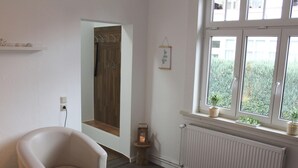 Uma sala de estar moderna com uma poltrona de couro branco, uma mesinha com garrafa e copos, um radiador e uma janela com plantas.