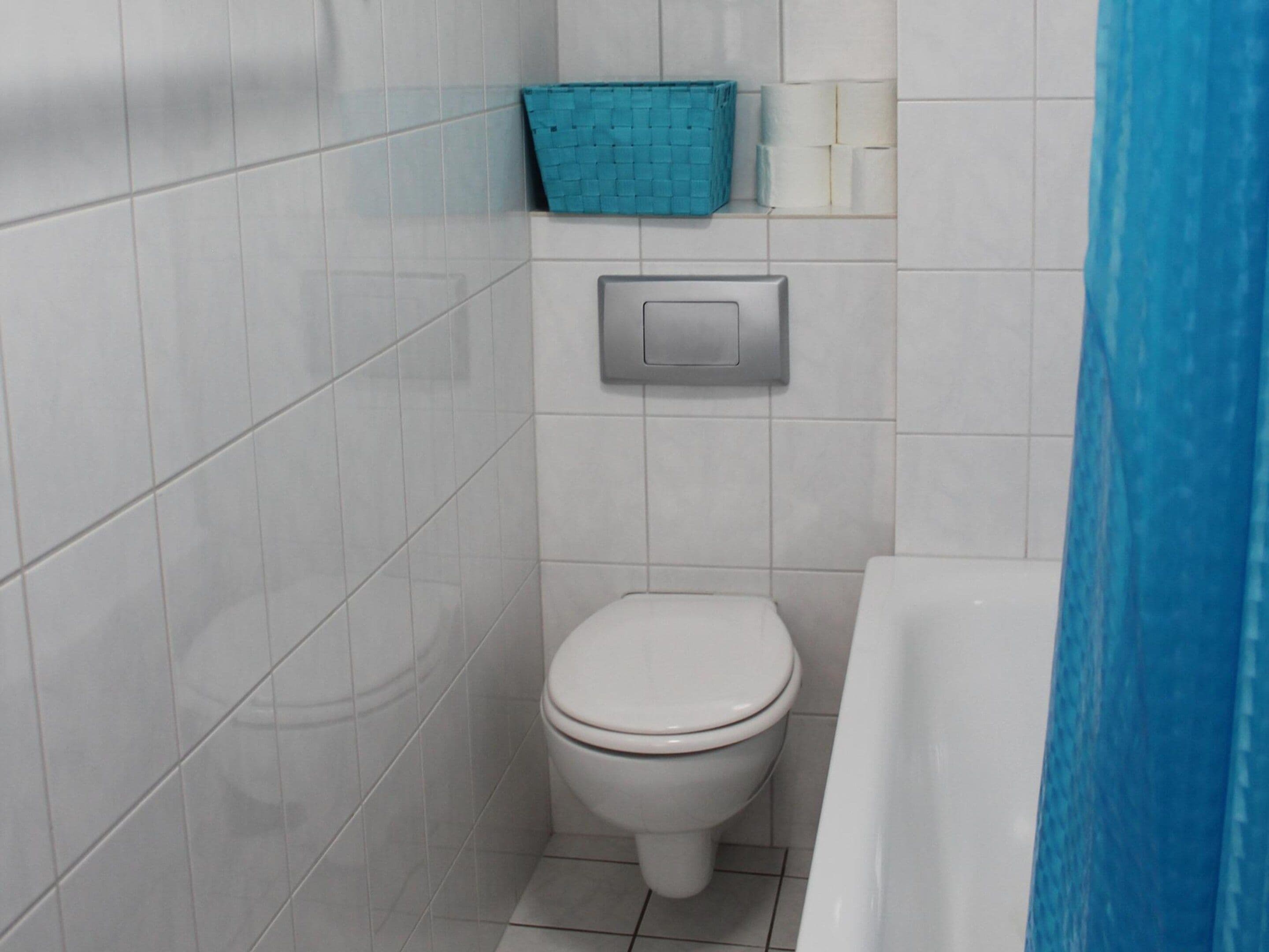 A small bathroom with a toilet, a blue basket, and a paper towel dispenser.