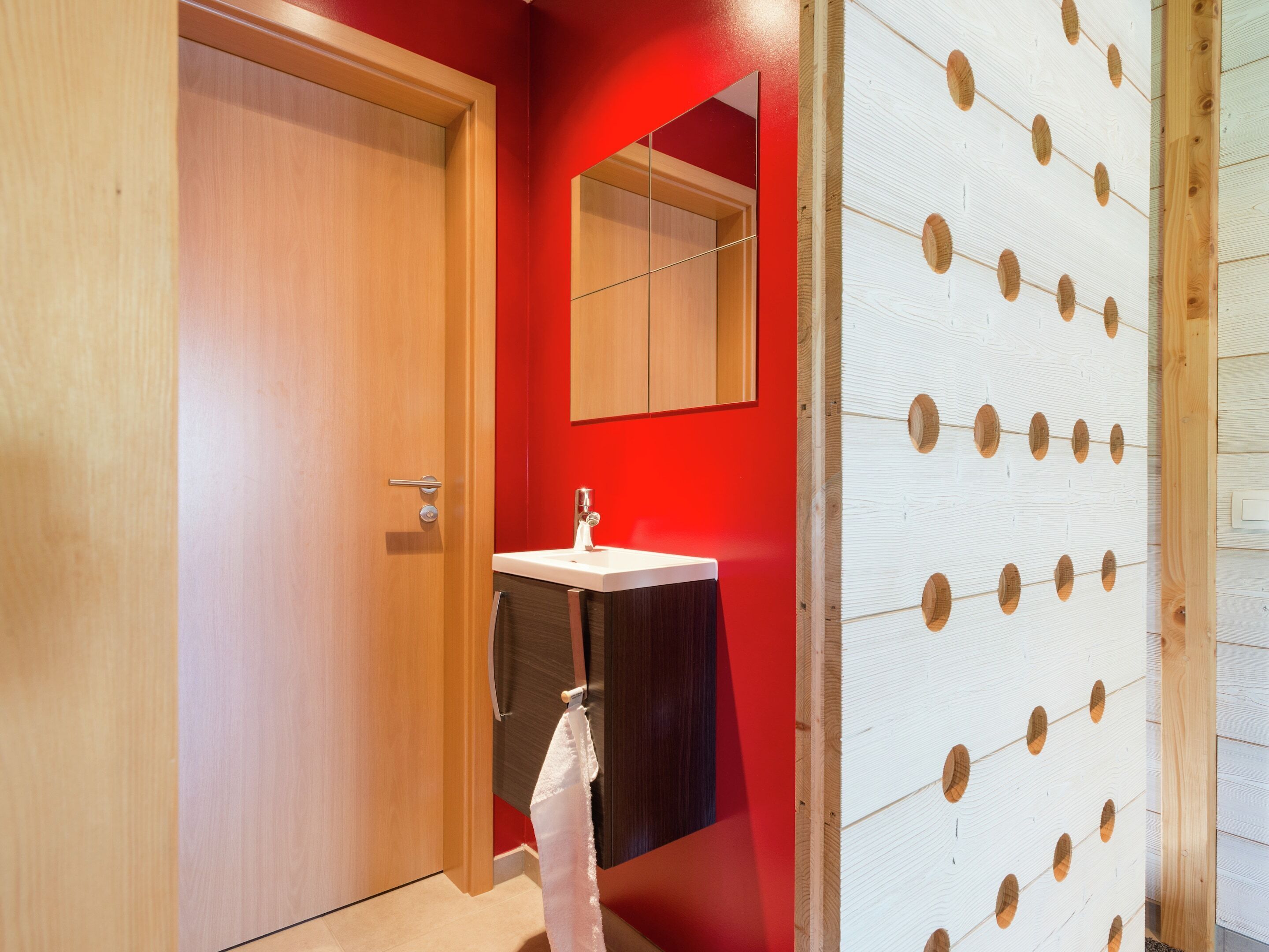 A bathroom with a wooden door, a white sink, and a red wall.