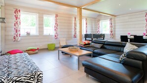 A spacious living room with a large black leather sofa, a wooden coffee table, and a zebra-patterned couch. There are two windows with floral curtains, a green chair, and a small table with a basket. - Rustic Retreat, Ovifat (Waimes)