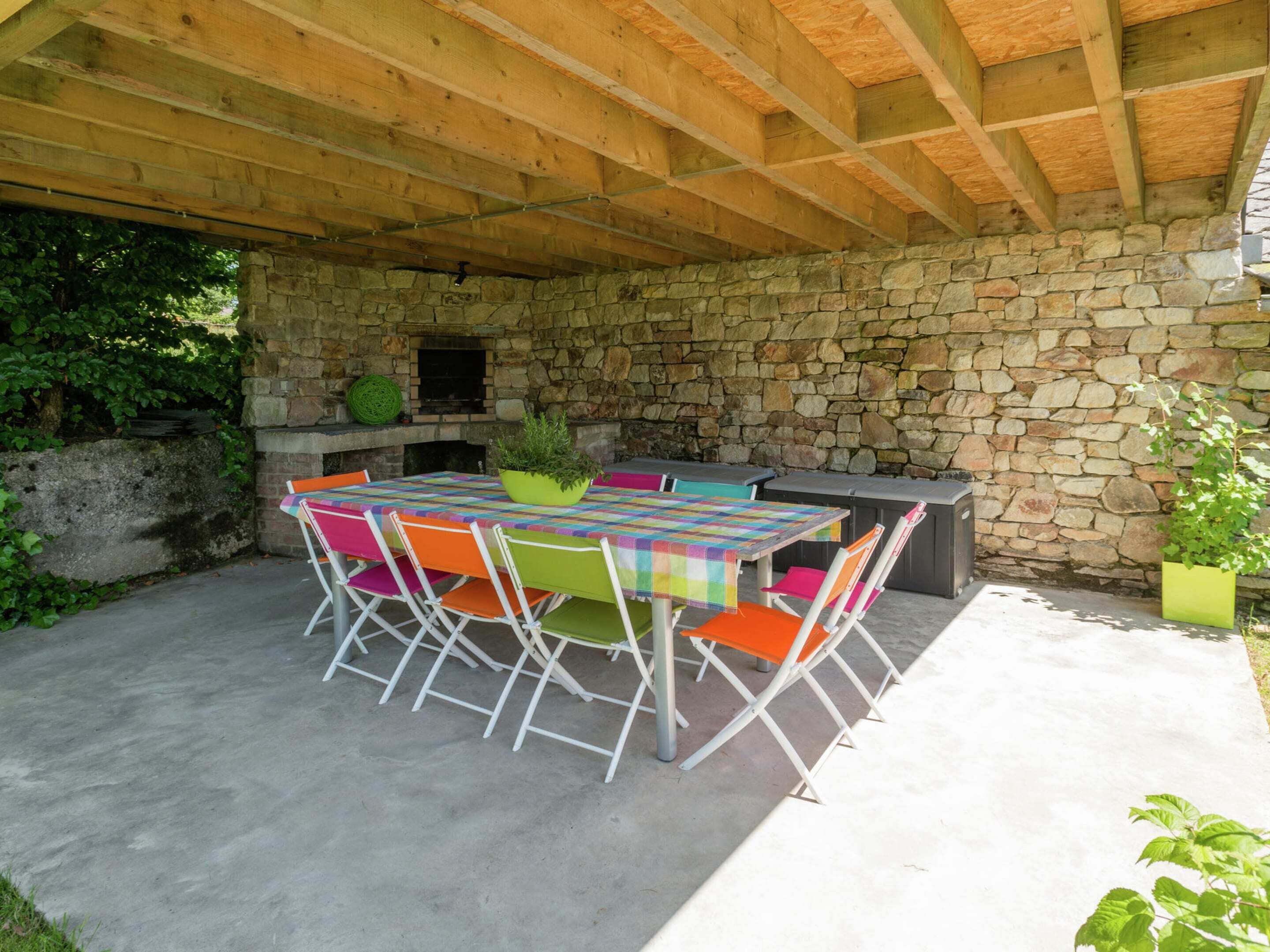 An outdoor patio with a stone wall, a wooden ceiling, and a table with colorful chairs.