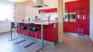 A modern kitchen with red cabinets, a stainless steel oven, and a bar area with stools. - Rustic Retreat, Ovifat (Waimes)
